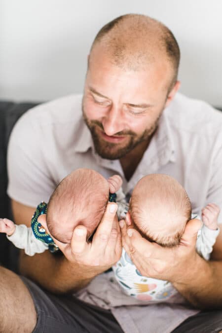 Vater hält die Köpfchen seiner Zwillinge in seinen Händen und schaut sie an