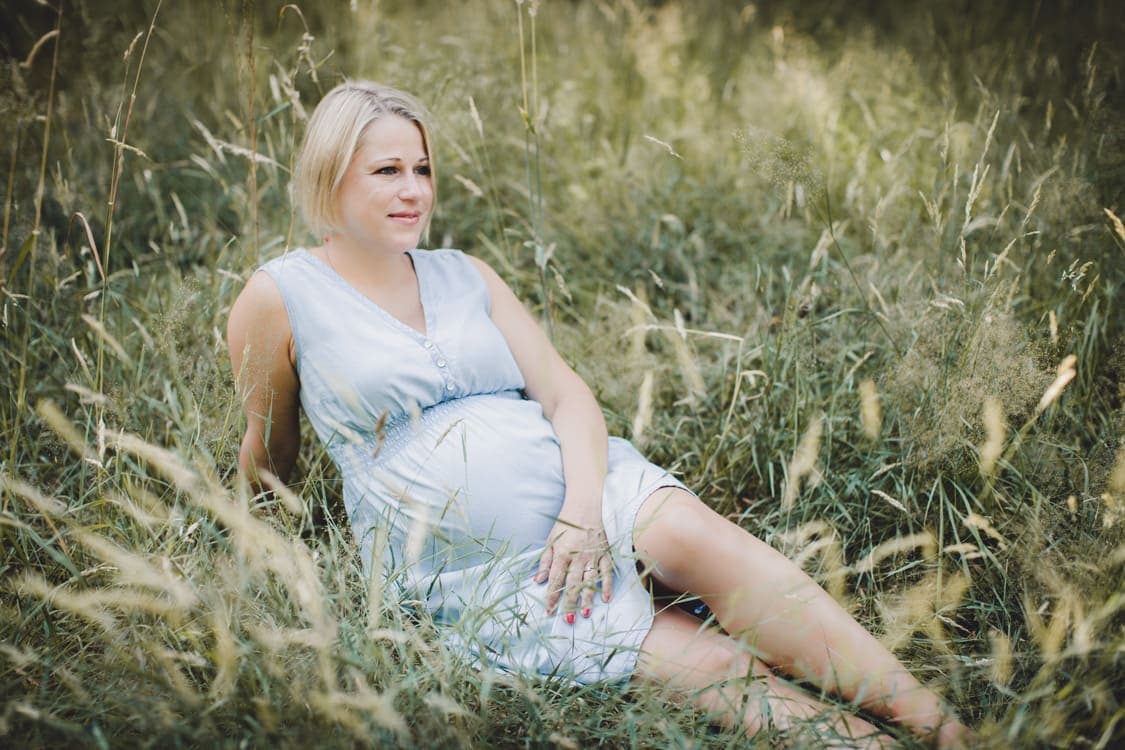 Frau mit Babybauch im hohen Gras