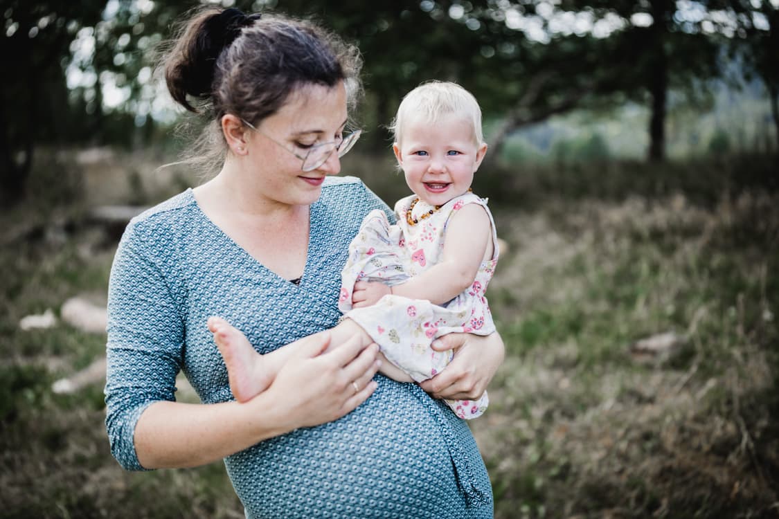 Schwangere Frau mit Tochter auf dem Arm