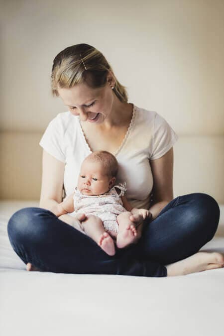 Mutter sitzt im Schneidersitz auf einem Bett und hält ihr Baby auf dem Schoß