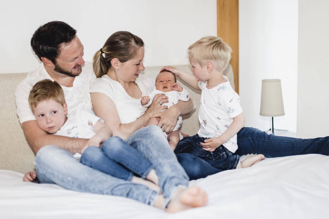 Familie mit Neugeborenem kuschelt zusammen auf einem Bett