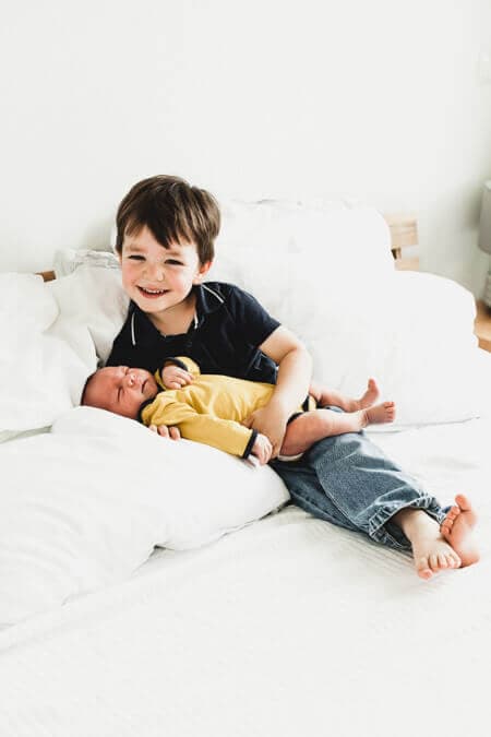 Junge hält seinen kleinen Bruder im Arm und sitzt dabei auf dem Bett