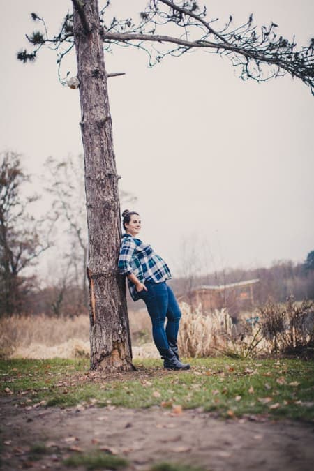 Schwangere Frau mit Karohemd lehnt an einem Baum