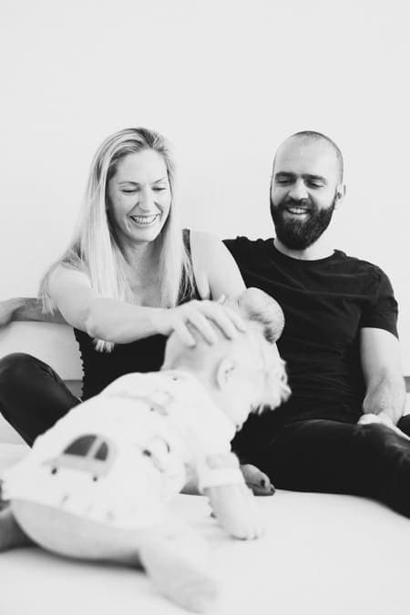 Familie sitzt auf dem Bett und kleiner Junge tollt herum