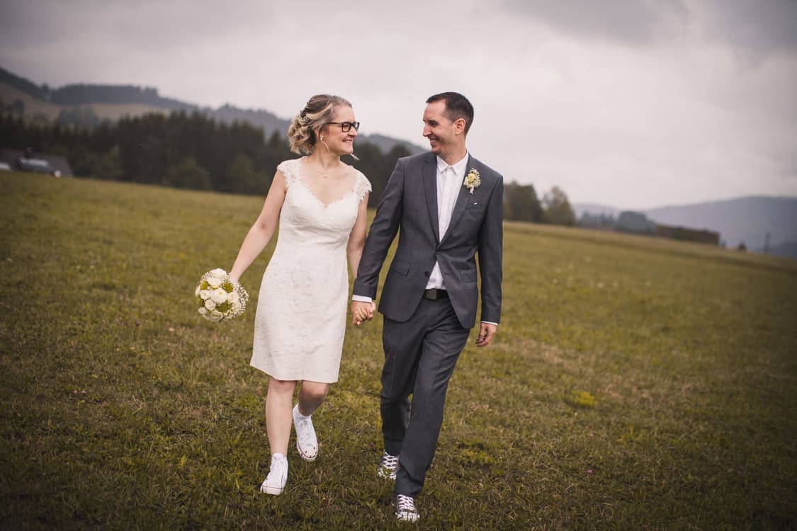 Brautpaar geht Hand in Hand über eine Wiese
