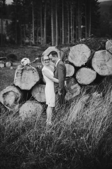 SW Foto von Brautpaar vor einem Stapel Baumstämmen