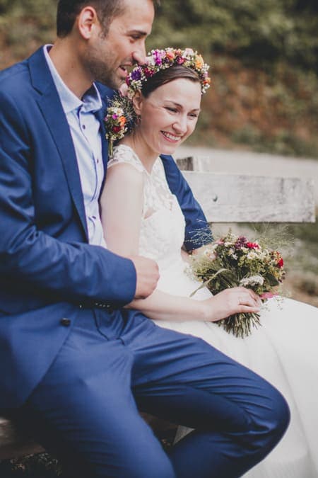 Brautpaar sitzt auf einer Bank. Bräutigam hält seine Braut dabei im Arm.