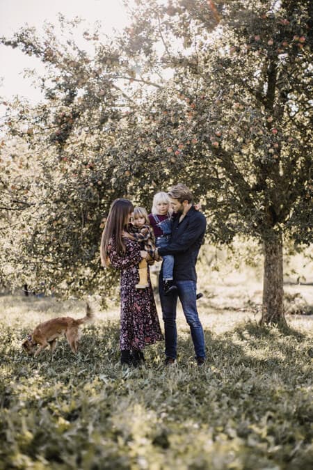 Familie mit Hund auf einer Wiese vor einem Apfelbaum