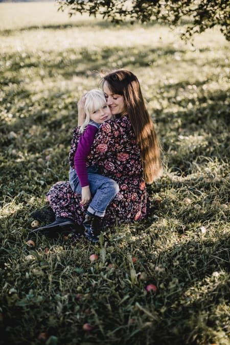 Mutter kuschelt mit ihrer Tochter auf dem Schoß auf einer Wiese