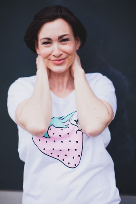 Frau mit Erdbeer T-Shirt streicht ihr Haar aus dem Gesicht und blickt in die Kamera