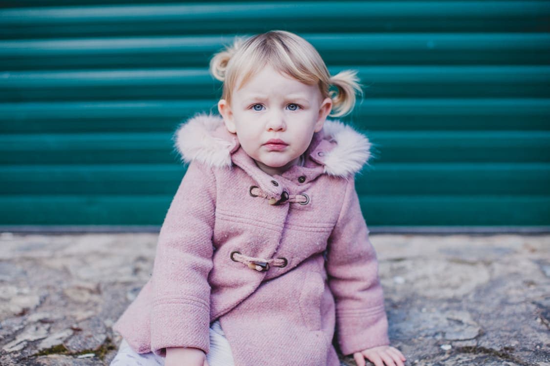 Mädchen mit rosaner Felljacke sitzt vor Rolltor