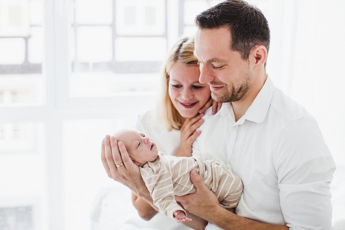 Eltern betrachten ihr Neugeborenes das der Vater im Arm Hält