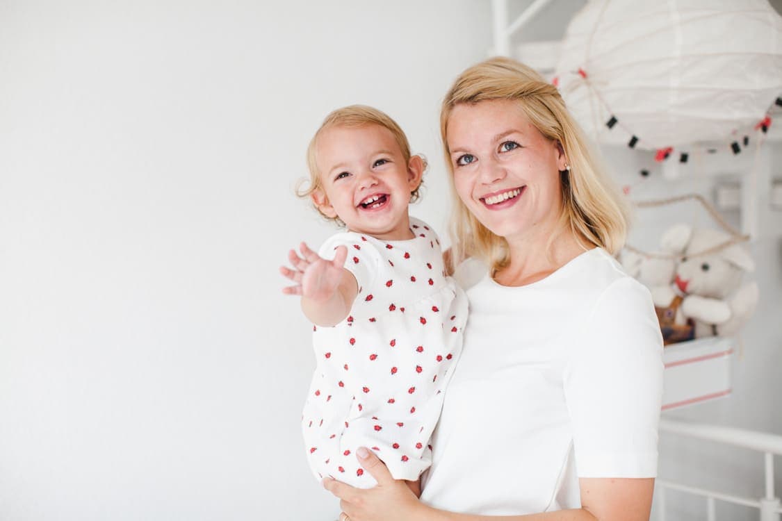 Mutter mit Tochter auf dem Arm. Mädchen streckt die Hand nach vorne. Beide lachen.