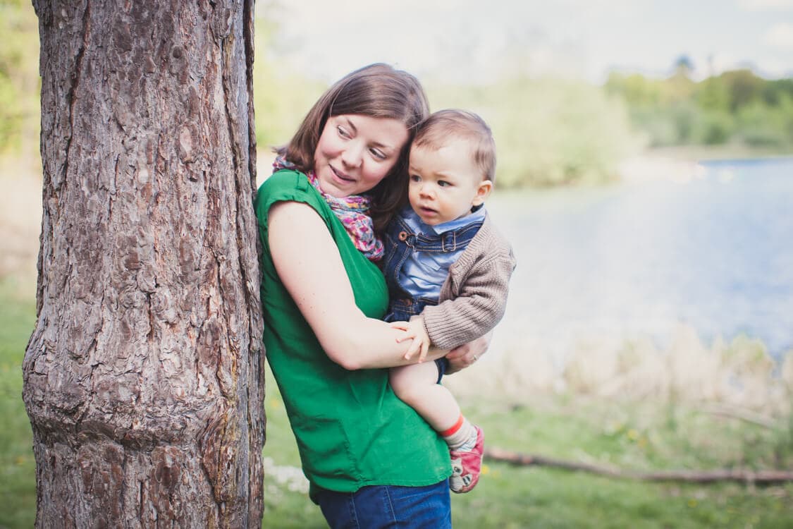 Mama lehnt mit kleinem Kind auf dem Arm am Baumstamm