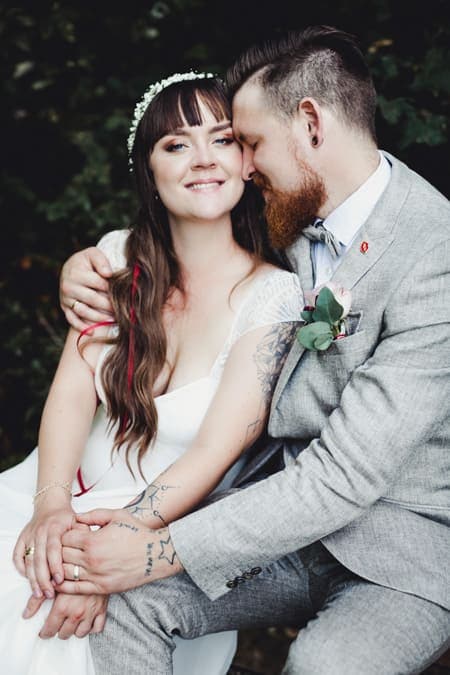 Brautpaar eng umschlungen auf eiiner Bank. Die Braut blickt in die Kamera.