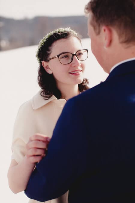 Braut vor Schneekulisse blickt Bräutigam an