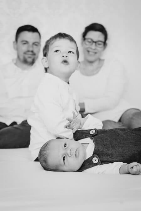 Familie sitzt auf dem Bett. Vor ihnen liegt das Baby.