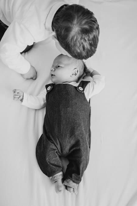 Baby liegt auf dem Bett. Bruder beugt sich über ihn.