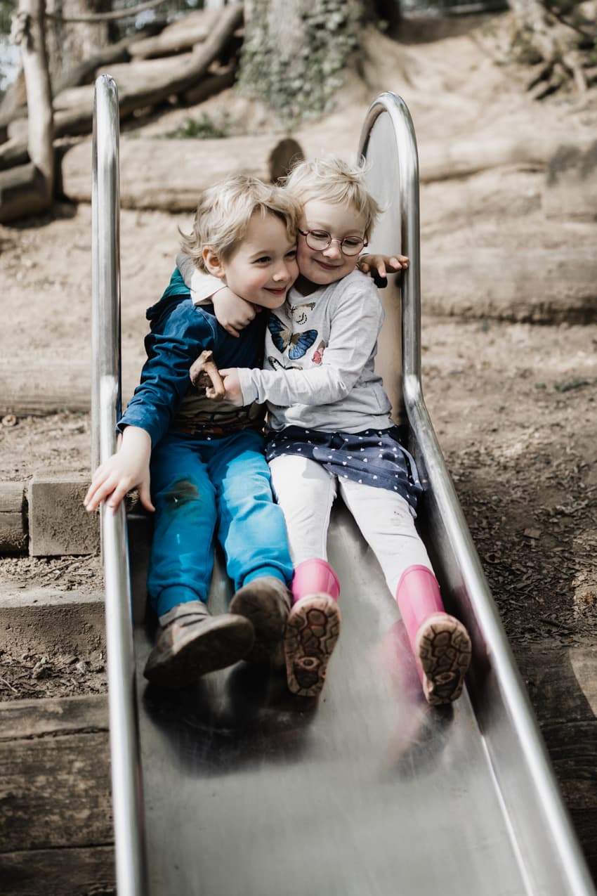 Geschwister auf einer Rutsche umarmen sich