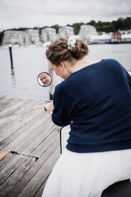 Braut sieht in den Rueckspiegel ihrer Vespa