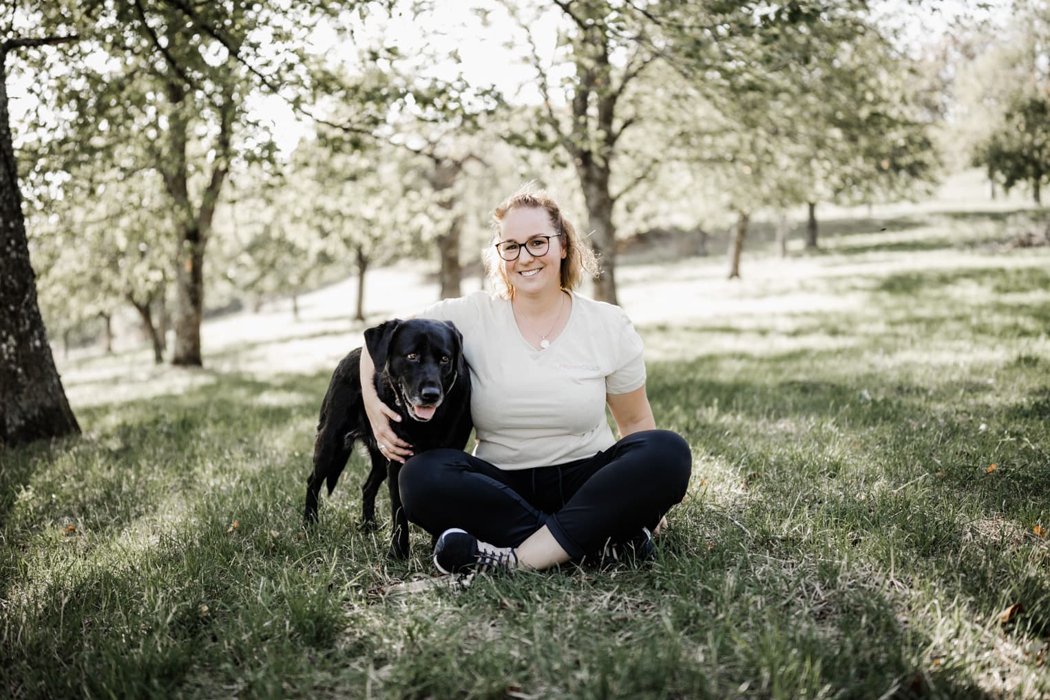 Frau sitz auf einer Wiese mit ihrem Hund unterm Arm