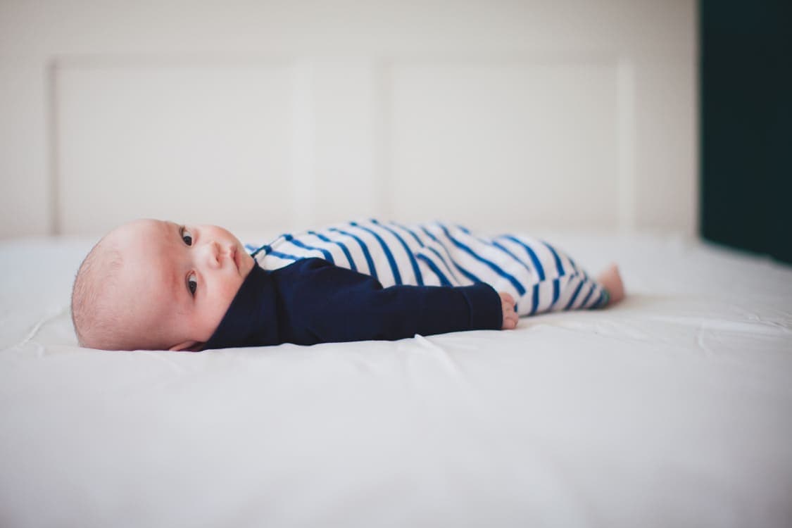 Baby liegt au einem Bett und blickt in die Kamera