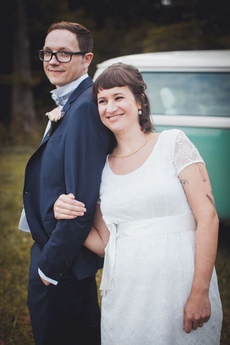 Braut leht an ihren Bräutigam vor einem Bulli