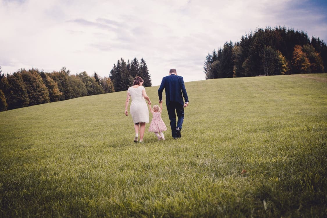 Brautpaar läuft mit Tochter an der Hand über eine Wiese