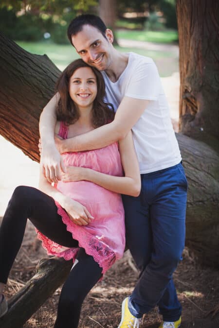 Schwangere Frau sitzt auf einem Ast ihr Mann umarmt sie von hinten