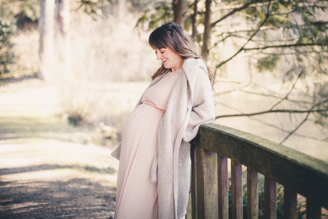 Frau mit Babybauch lehnt an einer Brücke
