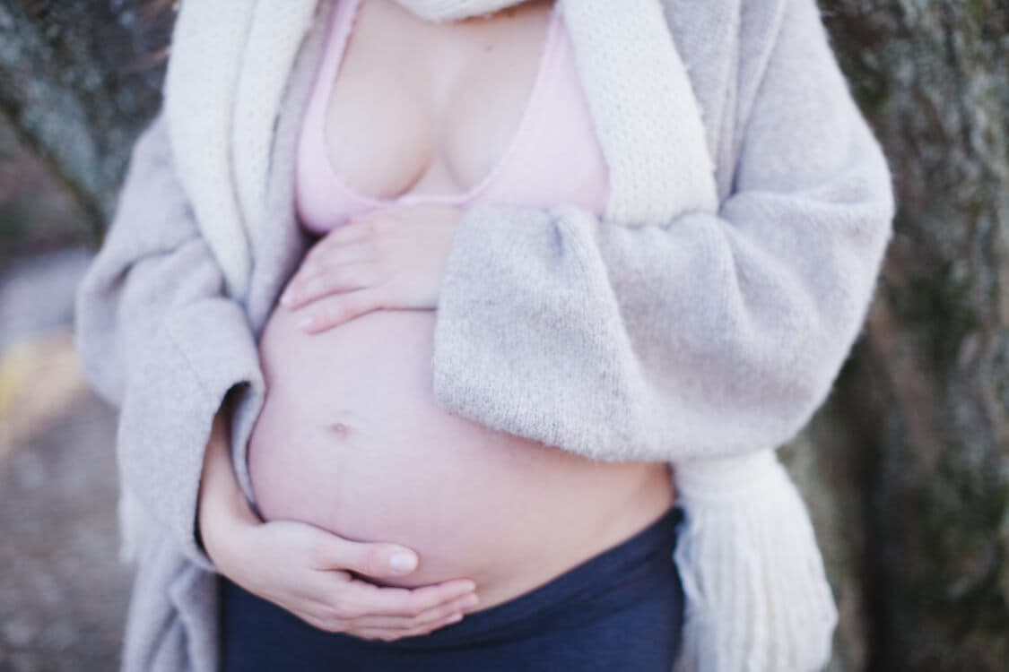 Nahaufnahme Babybauch mit Strickmantel und Schal