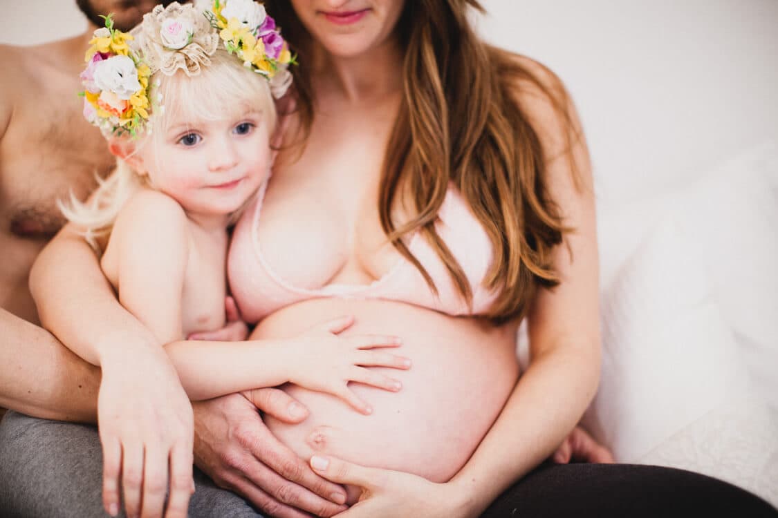 Mädchen mit Blumenkranz kuschelt mit Babybauch von Mama