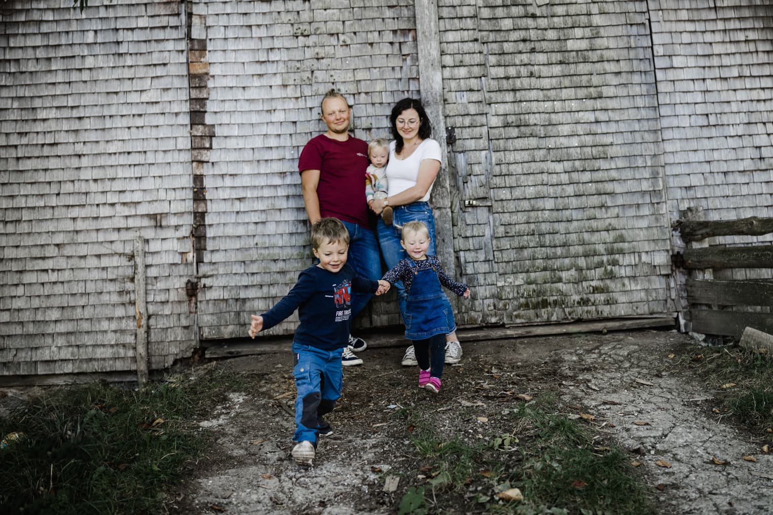 Kinder rennen hand in Hand. Eltern und Schwester stehen im Hintergrund.