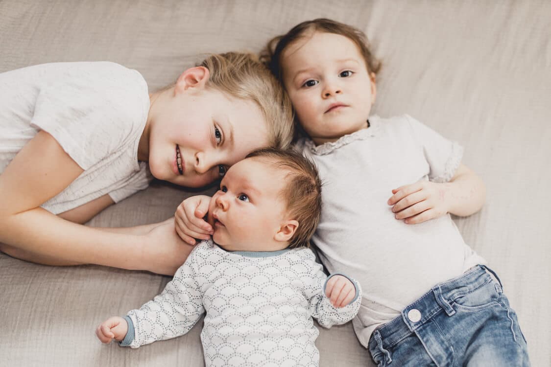 Drei Geschwister liegen eng mit ihren Köpfen beieinander