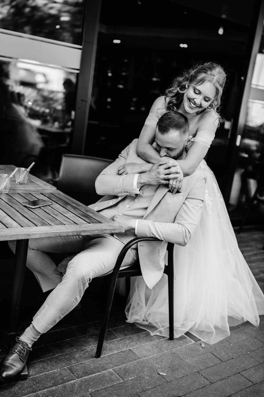 Braut umarmt Bräutigam von hinten im Café intime Hochzeitsfotografie Freiburg