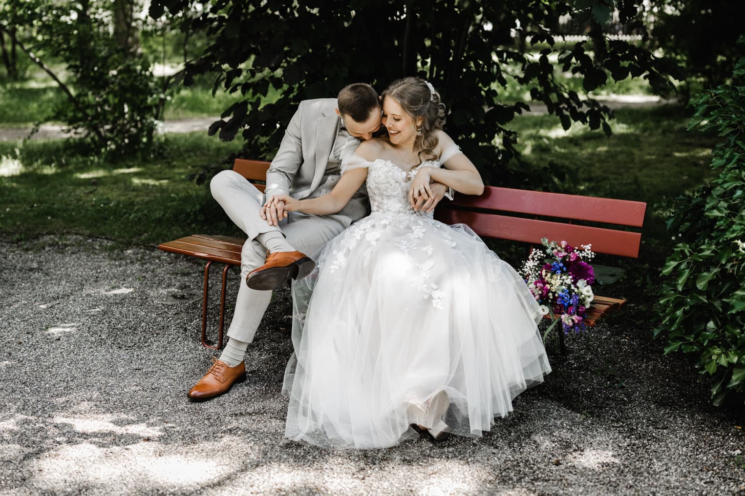 Brautpaar auf Bank, Bräutigam küsst Schulter romantische Hochzeitsfotografie