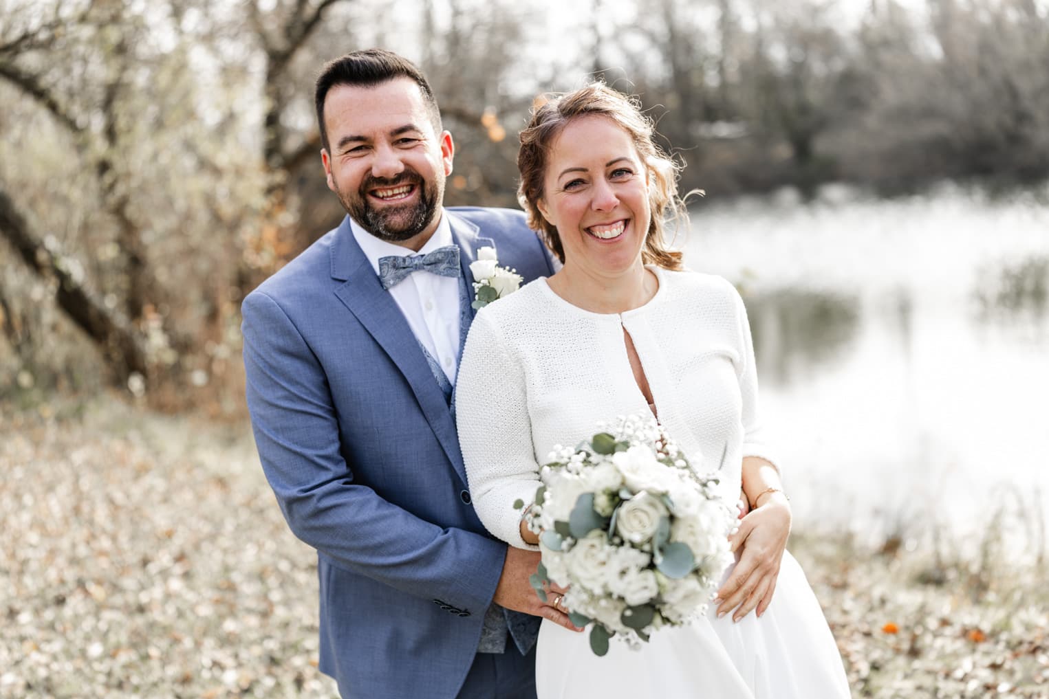Bräutigam umarmt die Braut von hinten am See, Hochzeitsfoto