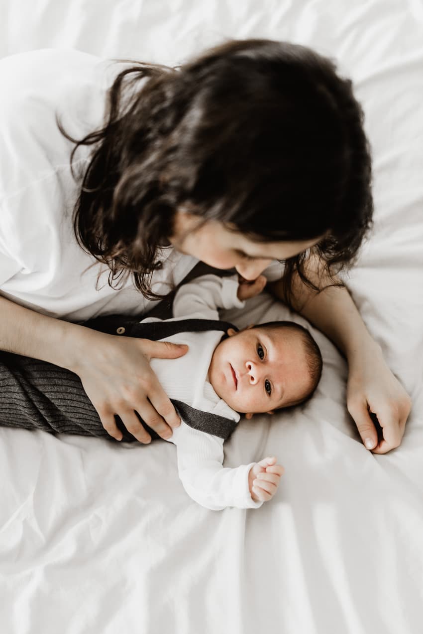 Mama kuschelt mit ihrem Baby auf dem Bett beim Neugeborenenshooting