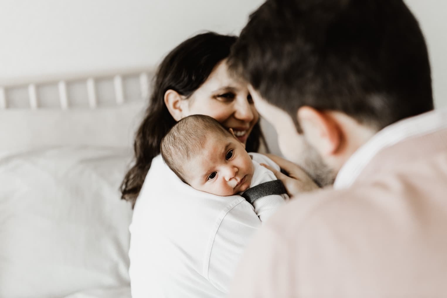 Baby liegt über der Schulter der Mutter und Papa ist im vordergrund, ruhige Homeshooting-Aufnahme