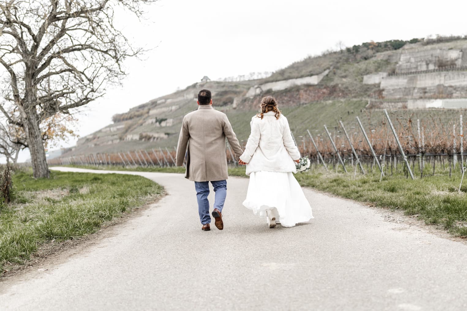 Brautpaar läuft Hand in Hand durch die Weinberglandschaft