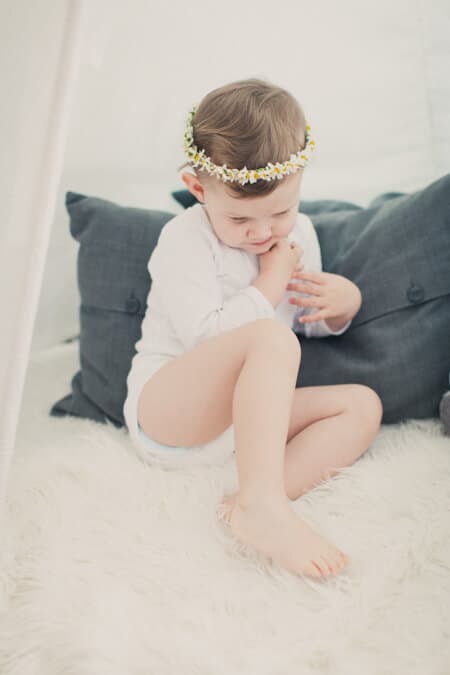 Mädchen mit Blumenkranz sitzt auf Schaffell