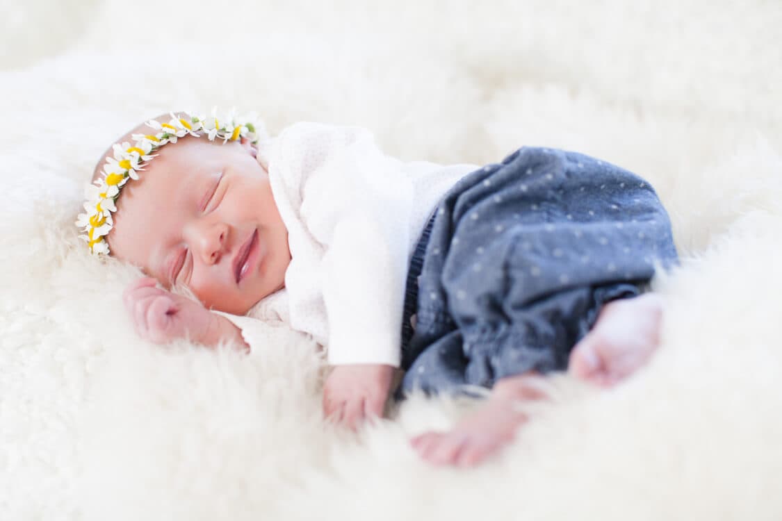 Neugeborenes mit Blumenkranz auf Schaffell